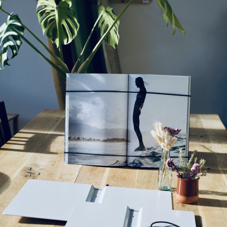 FOCUS | FRAME mit aufgeschlagenem Coffee Table Book auf dem Tisch, davor ein geöffneter Rahmen in Lichtgrau